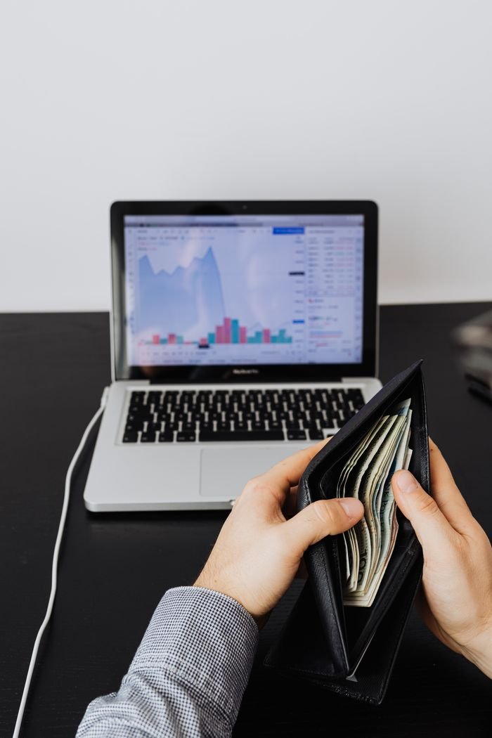 Mastering the First Impression: Your intriguing post title goes here A person holding a wallet filled with cash in front of a laptop displaying financial graphs and charts.