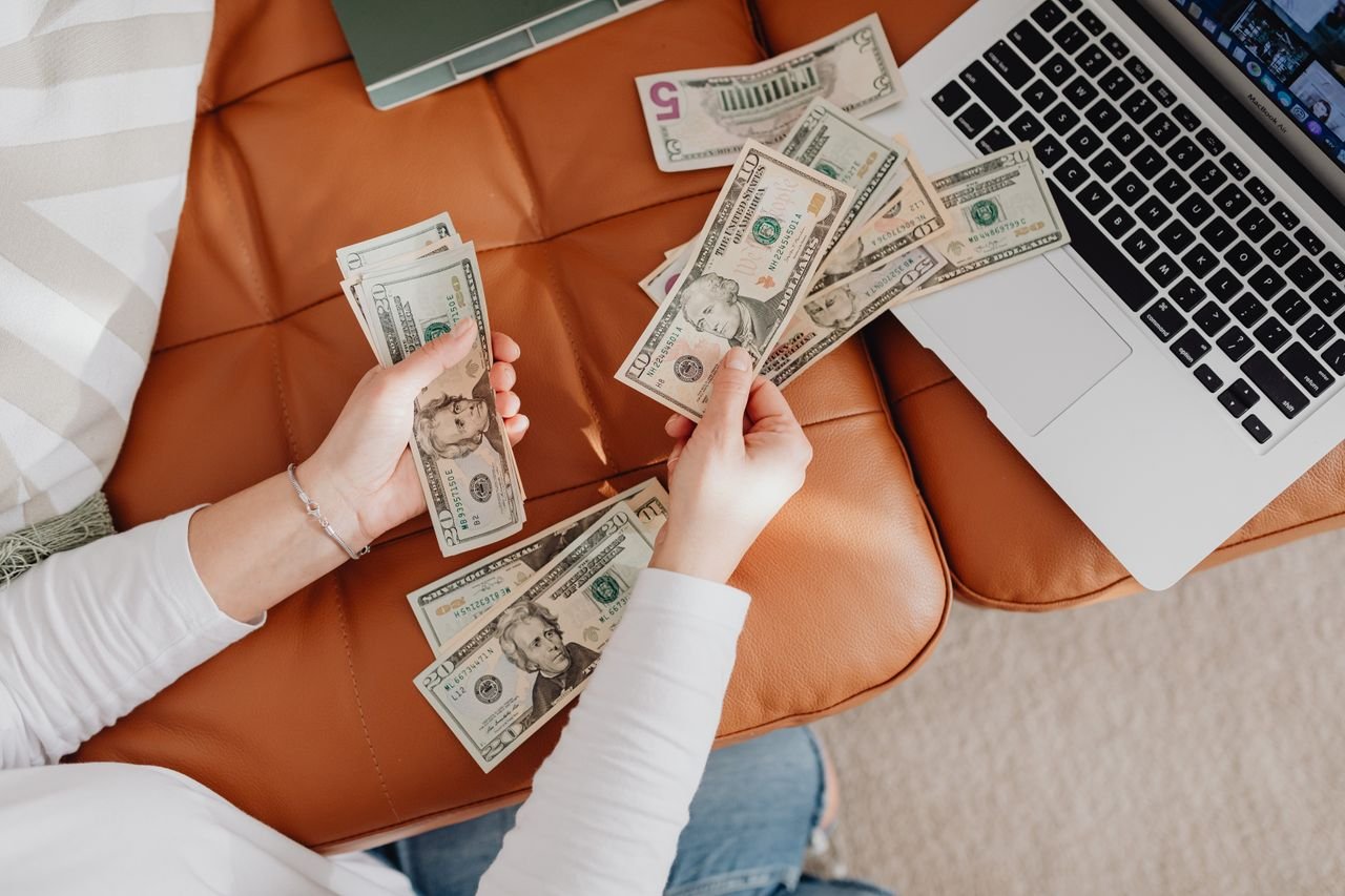 Crafting Captivating Headlines: Your awesome post title goes here A person counts US dollar bills on a couch with a laptop, symbolizing financial planning.
