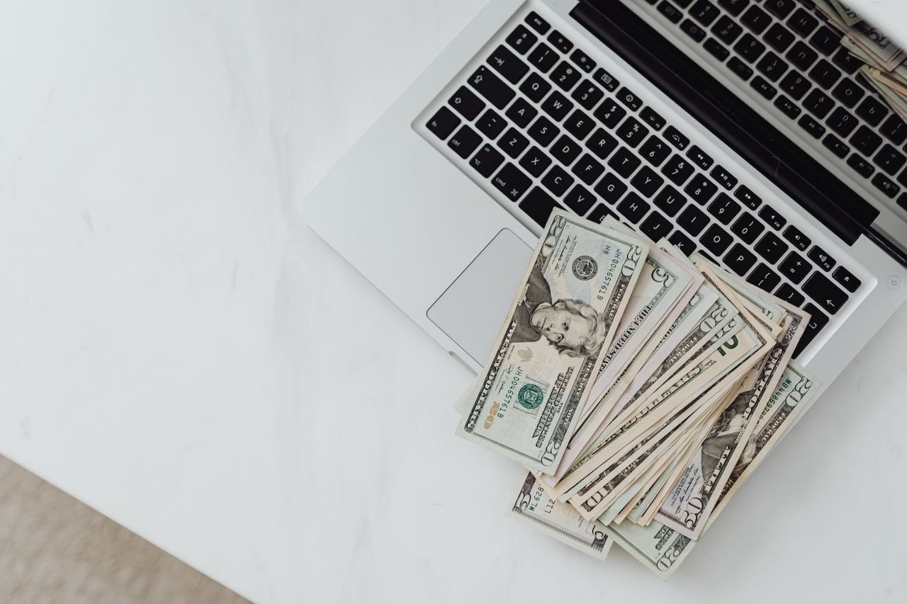 The Art of Drawing Readers In: Your attractive post title goes here Close-up of US dollar bills scattered on a laptop keyboard on a white desk, symbolizing digital finance.