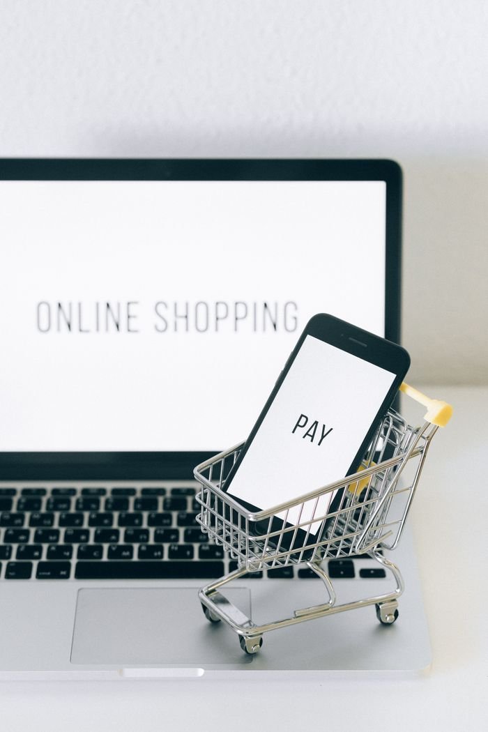 services-02 A smartphone in a miniature cart on a laptop symbolizes online shopping and digital payment.
