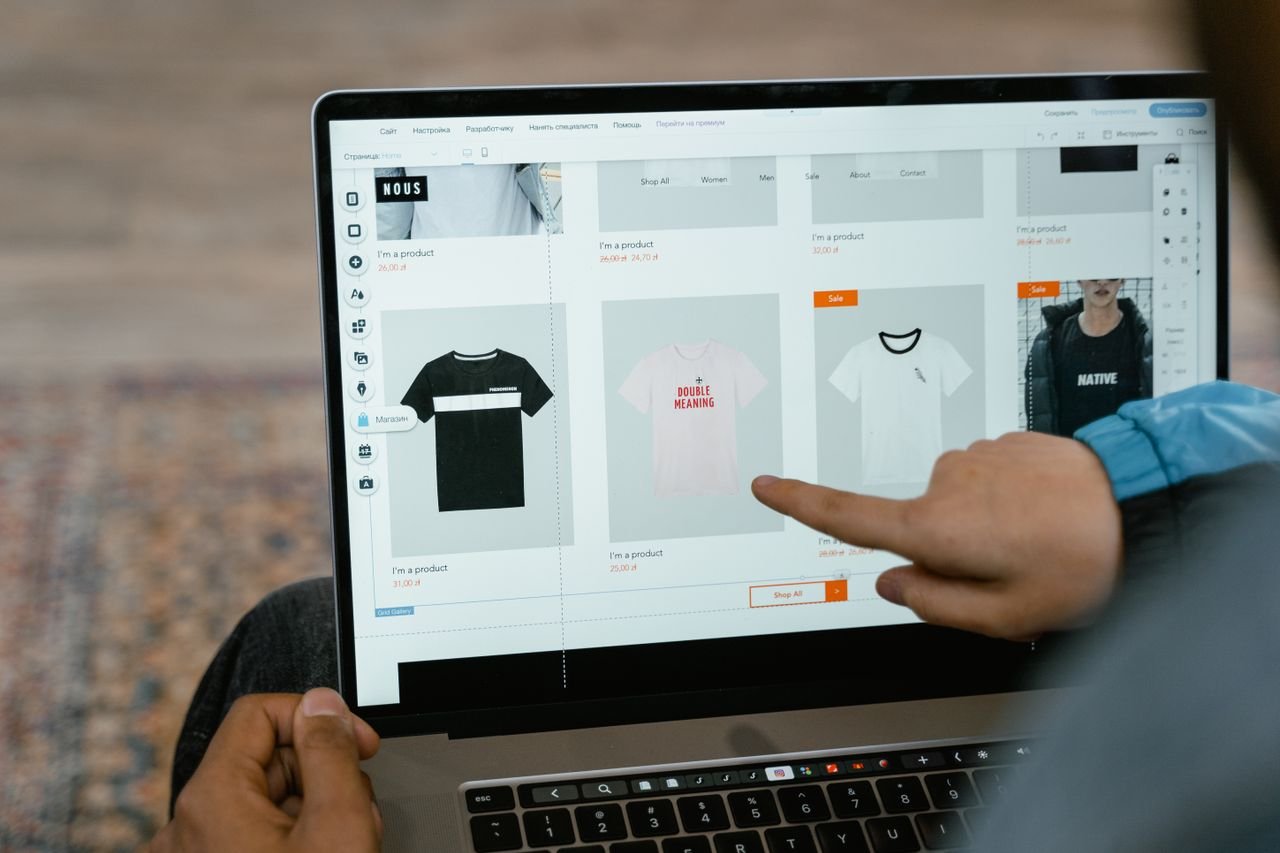 footer-02 A person points to t-shirt options in an online store on a laptop screen.